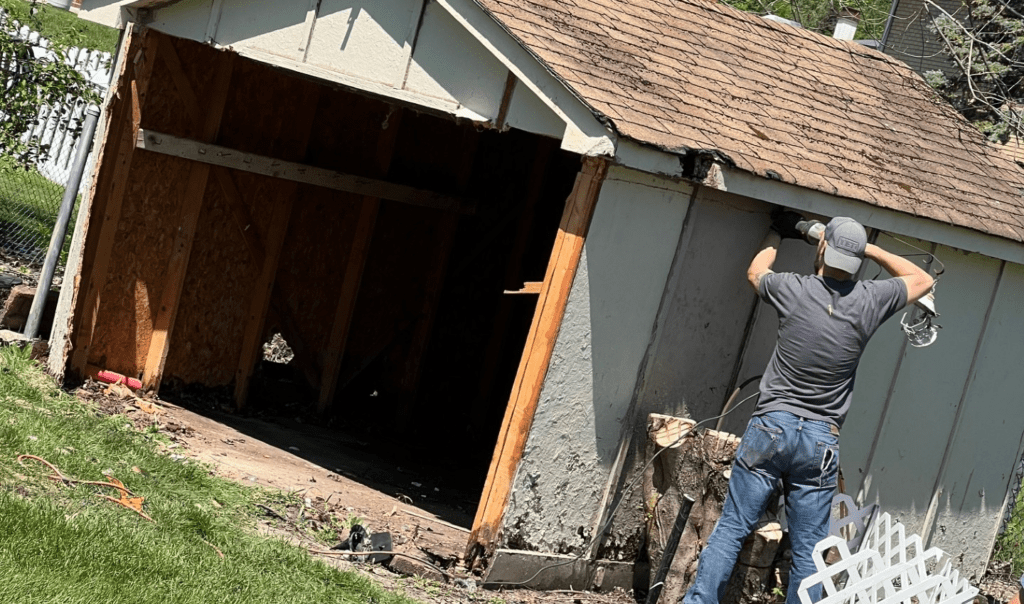 A person is demolishing a dilapidated shed, highlighting the need for a junk removal service to clear away the debris.